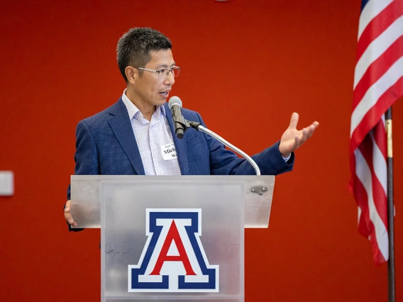 Michael Wu standing and speaking into a microphone, while standing in front of a podium with a "Block A" on it. 