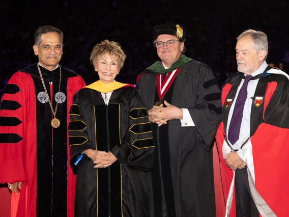 Four people standing and smiling in university graduation regalia 