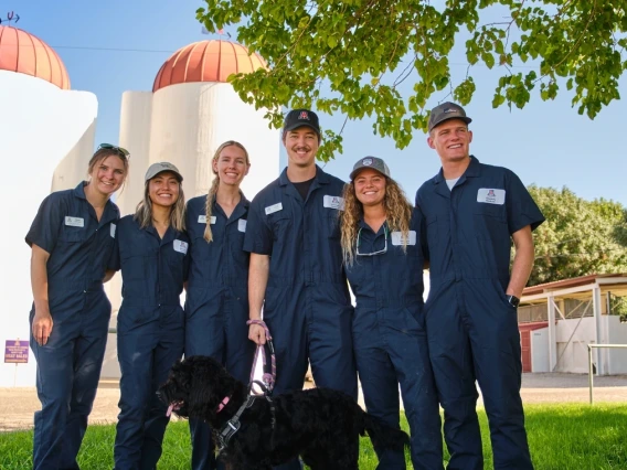 6 vet med students smile on farm with leashed black lab 