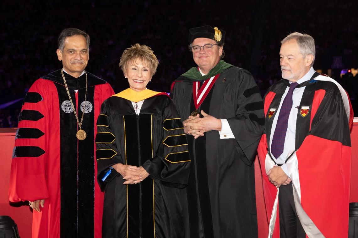 Four people standing and smiling in university graduation regalia
