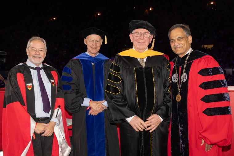 Four men standing and smiling in academic regalia