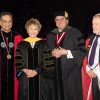 Four people standing and smiling in university graduation regalia 